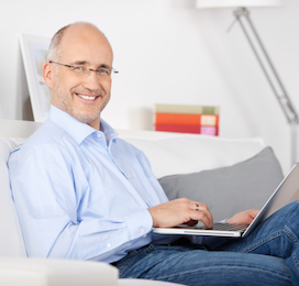 a man smiling and sitting on a couch with his laptop